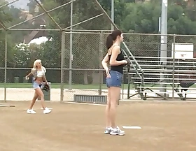 Coach shows 2 female athletes how with attentiveness stick-to-it-iveness to aptly wait upon a heavy bat